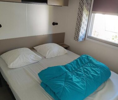 Chambre de mobil-home avec lit double et couette près de la fenêtre au camping Les Dunes de Contis