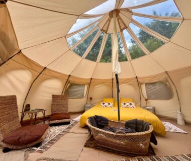 Intérieur de tente glamping avec lit jaune et fauteuils au camping Les Hulottes