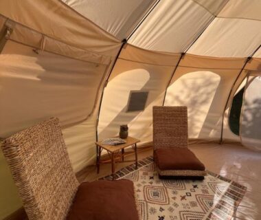 Intérieur de tente avec fauteuils en osier et tapis au camping Les Hulottes