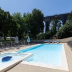 Piscine extérieure avec transats et viaduc en arrière-plan au camping Les Rives d'Auzon confort 6 pers