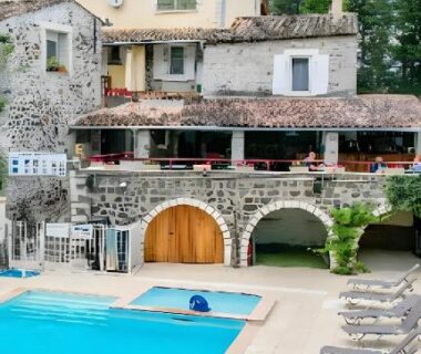 Piscine extérieure avec transats devant bâtiment en pierre du camping Les Rives d’Auzon confort 6 pers