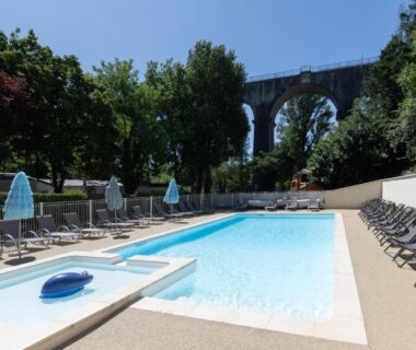 Piscine extérieure avec transats et viaduc en arrière-plan au camping Les Rives d'Auzon confort 6 pers