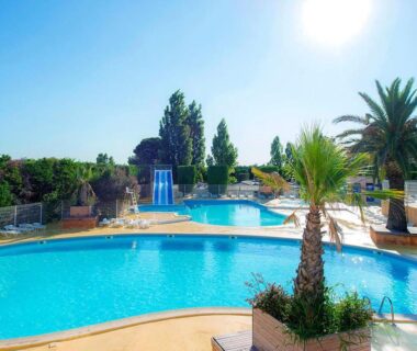 Piscine extérieure avec palmiers et toboggan au camping Les Salins de la Gardiole