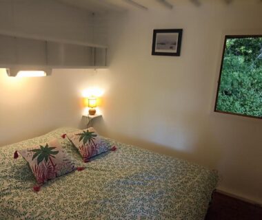 Chambre avec lit double lampe chevet et fenêtre sur végétation dans les cabanes de l'île aux oiseaux Guern
