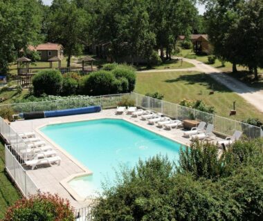 Piscine extérieure avec transats et chalets en arrière-plan au camping Les chalets de Dordogne