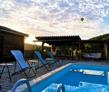 Piscine et transats avec montgolfières au coucher du soleil au camping Les nids de Bonnan