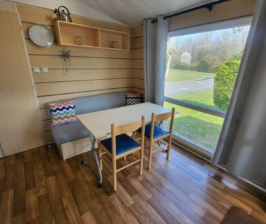 Coin repas avec grande fenêtre donnant sur l'extérieur du Mobil home Les pieds dans l'Orne