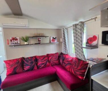 Salon de mobil-home avec canapé rouge et kitchenette au camping Les sables du midi