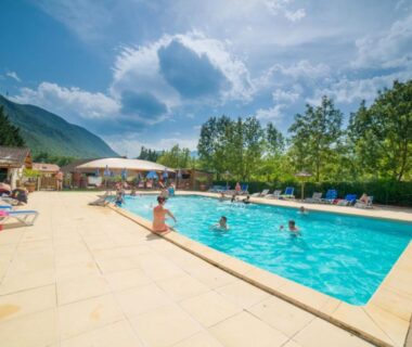 Piscine extérieure entourée de transats et montagnes au camping L'imprévu
