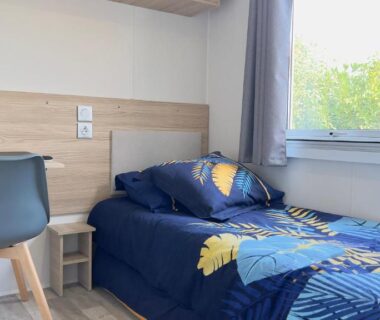 Chambre avec lit simple bureau et fenêtre sur verdure dans L'incontournable Tout Confort Camping Siblu
