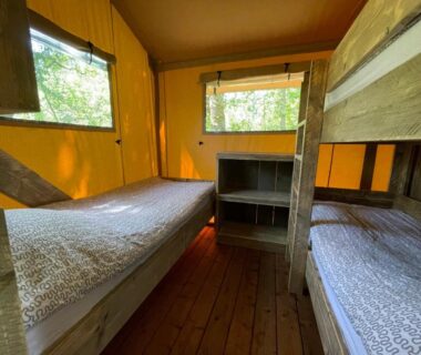 Intérieur d'un lodge avec lits superposés en bois et fenêtres donnant sur la forêt aux Lodges du Bois Dodo