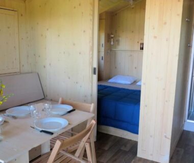 Coin repas et chambre en bois avec douche visible dans les Lodges du Ushuaïa Villages Camping les 4 Saisons