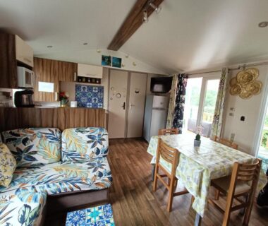 Salon avec canapé table et kitchenette dans le Logement 3 chambres Vue Lac Camping 4 étoiles Foix