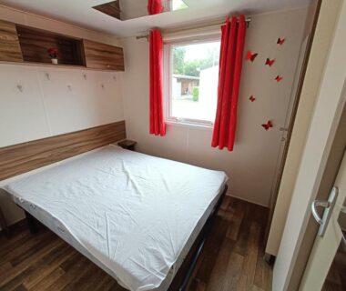 Chambre avec lit double et rideaux rouges dans le Logement 3 chambres Vue Lac Camping 4 étoiles Foix