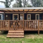 Terrasse couverte en bois avec mobilier et marches devant mobil-home dans le camping L'orée du bois