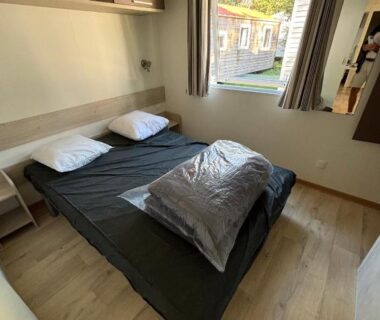 Chambre intérieure avec lit double et fenêtre donnant sur les mobil-homes du camping Louisiane 1