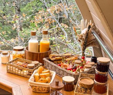 Table en bois avec viennoiseries confitures et jus devant fenêtre sur la forêt au Lov'nid spa et sauna