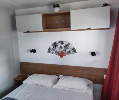 Chambre avec lit double rangement mural et rideau rouge au camping MAR ESTANG