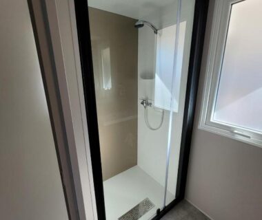 Salle de bain avec cabine de douche vitrée et fenêtre dans le mobil home MH 170