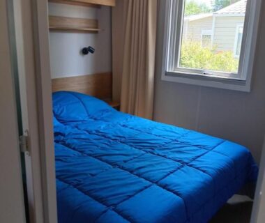 Chambre double avec lit bleu et fenêtre donnant sur le camping dans le MH 229