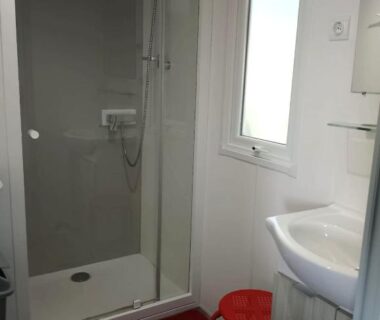 Salle de bain avec cabine de douche et petit tabouret rouge dans le MH 414 SAMBA