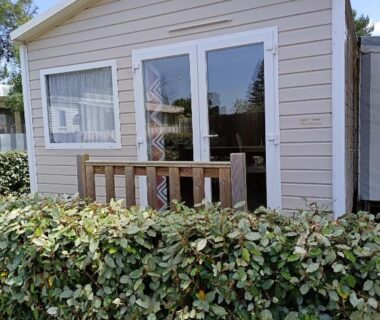 Devant la façade avec baie vitrée et haie du mobil-home MH 805 Camping Bois Dormant