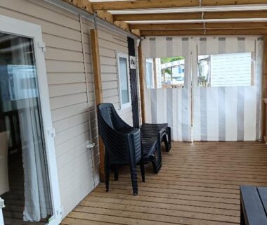 Terrasse couverte avec chaises empilées et porte fenetre sur plancher bois du MH F101 Camping Bois Masson