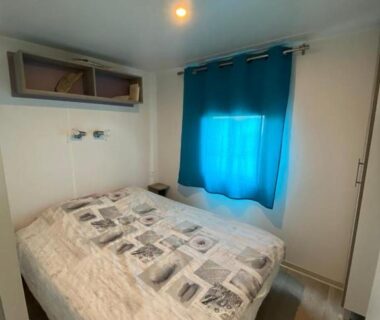 Chambre avec lit double et rideau bleu dans le mobil home MH148 du camping NOVELA