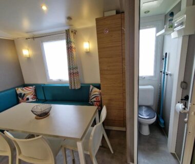 Intérieur coin repas avec table chaises banquette et salle d'eau visible dans le mobil home MH2-CONFORT