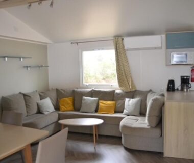 Salon avec canapé et kitchenette dans le mobilhome MHT20 3 chambres et 2 sdb dans camping 4 étoiles
