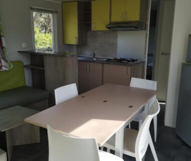 Intérieur avec table, chaises et kitchenette dans le mobil home 3 chambres du Camping La Pommeraie Trégunc
