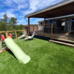 Terrasse avec pelouse synthétique, toboggan et transats du MOBIL HOME 40M2 ECRIN DE VERDURE