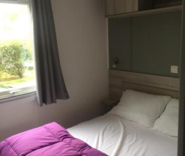 Chambre avec lit et couette près d'une fenêtre dans le MOBIL HOME 6/8 places