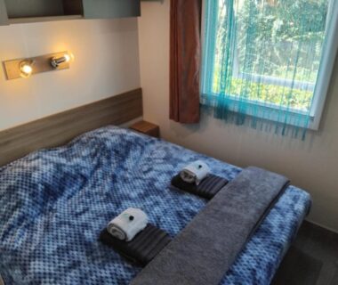 Chambre avec lit double couette bleue serviettes pliées dans le MOBIL HOME GLAMPING CONFORT