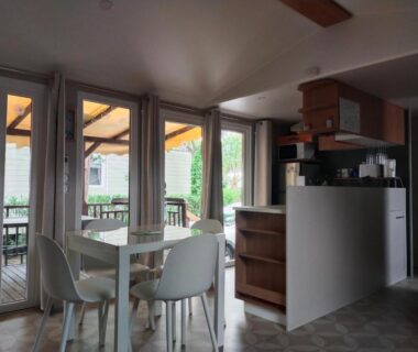 Séjour avec table et baie vitrée donnant sur terrasse du mobil home Le Lozérien