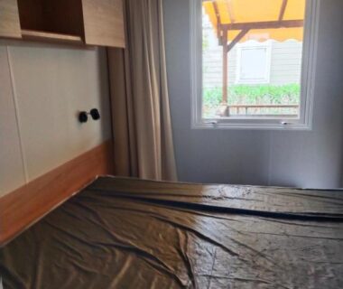 Chambre avec lit et fenêtre donnant sur terrasse du mobil home Le Lozérien