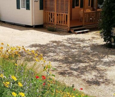 Terrasse en bois et allée gravillonnée bordées de fleurs du mobilhome 3 chambres