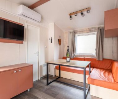 Mobil-home intérieur avec banquette table et télévision au Maïana Resort