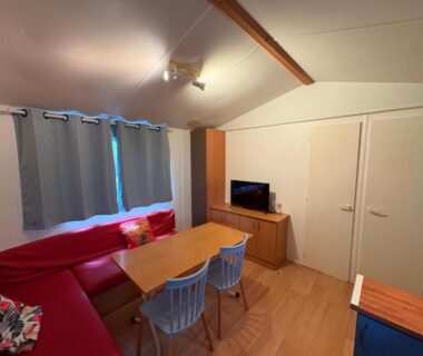 Salon avec banquette rouge table et télévision dans les Bungalows Manoir le Mingreaud