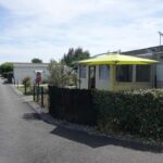 Terrasse avec parasol jaune et haie du Mobil-Home 54 au Parc Résidentiel de la Plage 4 personnes