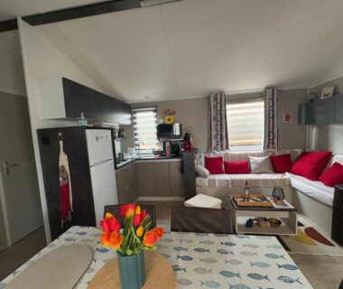 Salon avec canapé rouge et cuisine ouverte dans le Mobil-Home 6 personnes