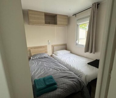 Chambre intérieure avec deux lits serviettes pliées et fenêtre dans le Mobil-Home