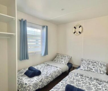 Chambre avec deux lits simples et rideaux bleus dans le Mobil Home Abricotiers 1