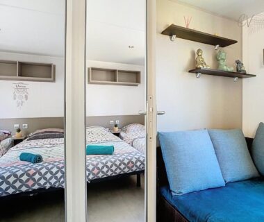 Intérieur avec lit, banquette bleue et miroir du mobil-home CL 14 à Vias La Carabasse