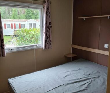 Chambre avec lit et fenêtre donnant sur des mobil-homes dans le Mobil Home Camiers