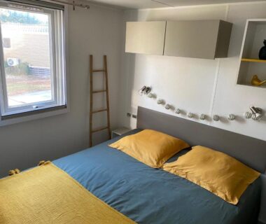 Chambre avec lit double et linge jaune et bleu dans le Mobil-Home Camping Club 5* Montalivet