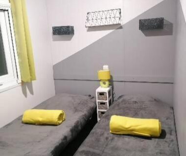 Chambre avec deux lits simples rideau jaune et chevet du Mobil-Home Cosy Climatisé 3 chambres