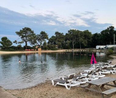 Plage avec transats et parasols au bord du plan d'eau du Mobil Home FI11 Camping les Viviers