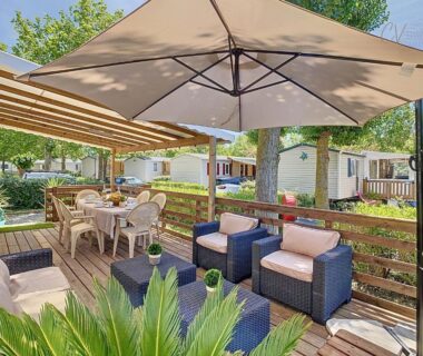 Terrasse extérieure avec salon et parasol du Mobil-Home JA 85 à Vias La Carabasse Camping Siblu avec piscine payante