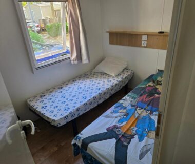 Chambre avec deux lits simples et fenêtre dans le Mobil-Home La Carabasse